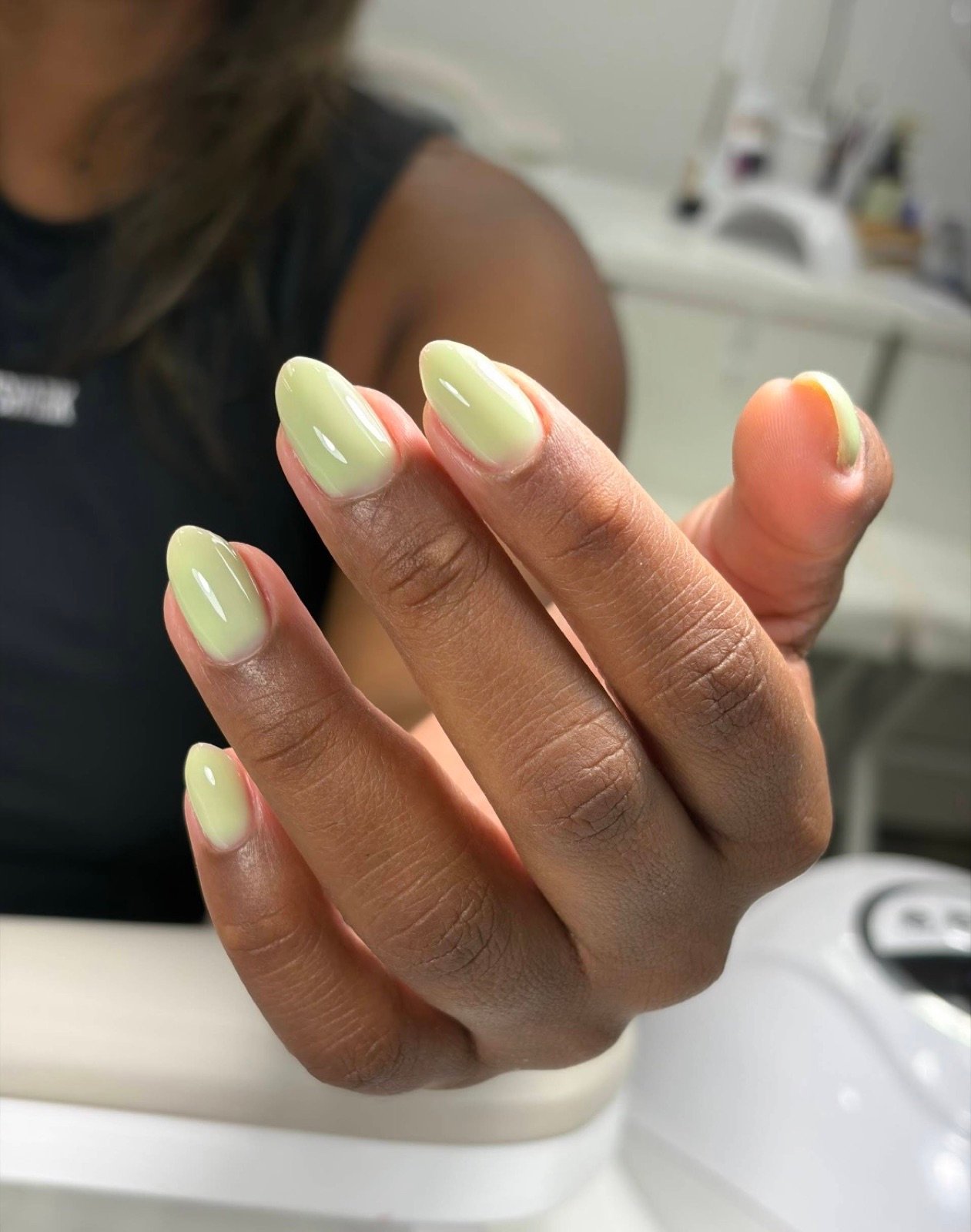 Nail design inspiration for dry manicure Tampa: Close-up of a hand with neatly manicured pale green oval-shaped nails in a professional salon setting
